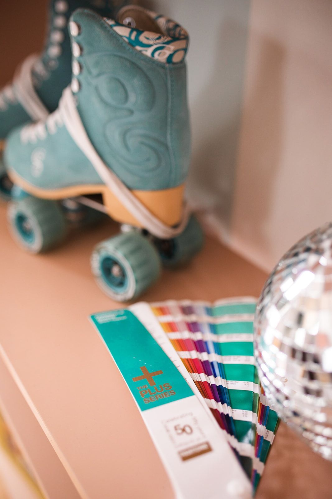 Teal roller skates, paint swatches, and disco ball on a pink shelf.