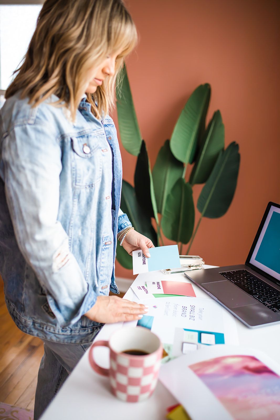 A woman is standing at a desk with a laptop and a cup of coffee.