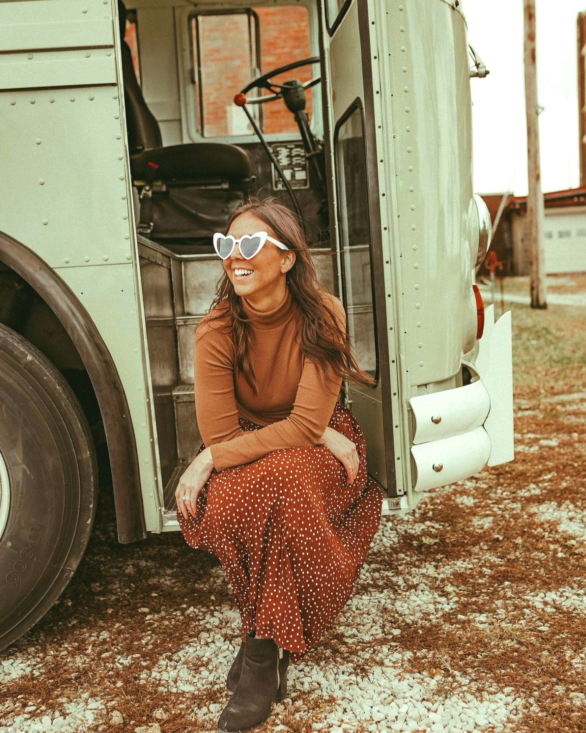 A woman wearing sunglasses is kneeling in front of a bus.