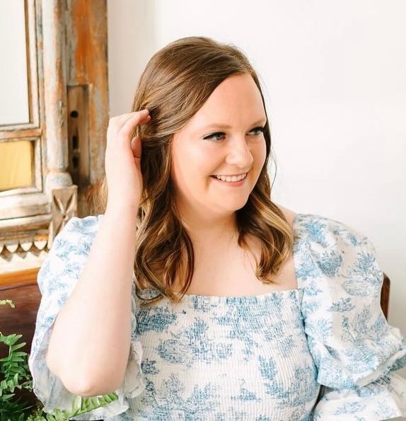 A woman in a blue and white dress is sitting in a chair and smiling.