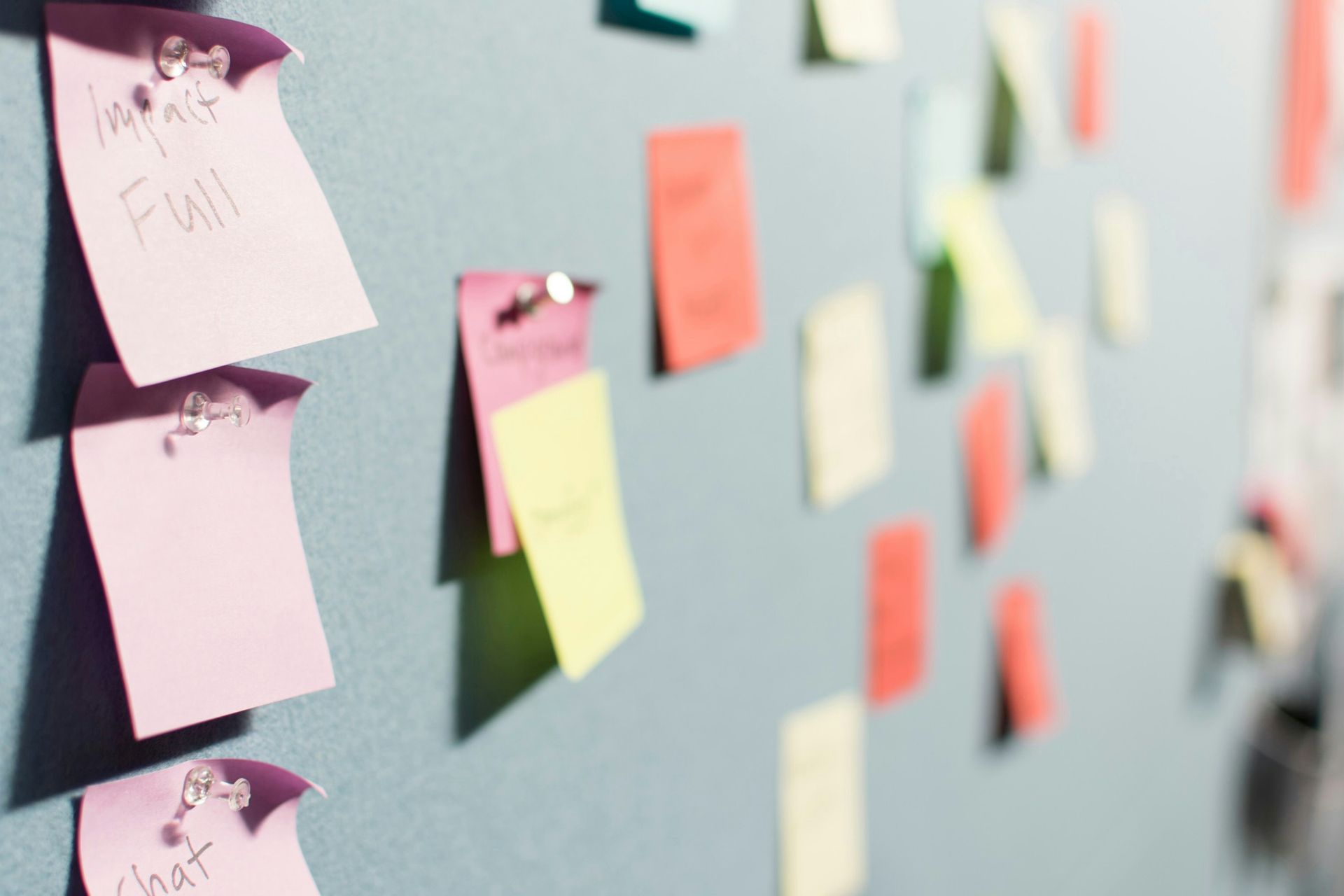 Colorful post-it notes organized and pinned with push pins on a wall 