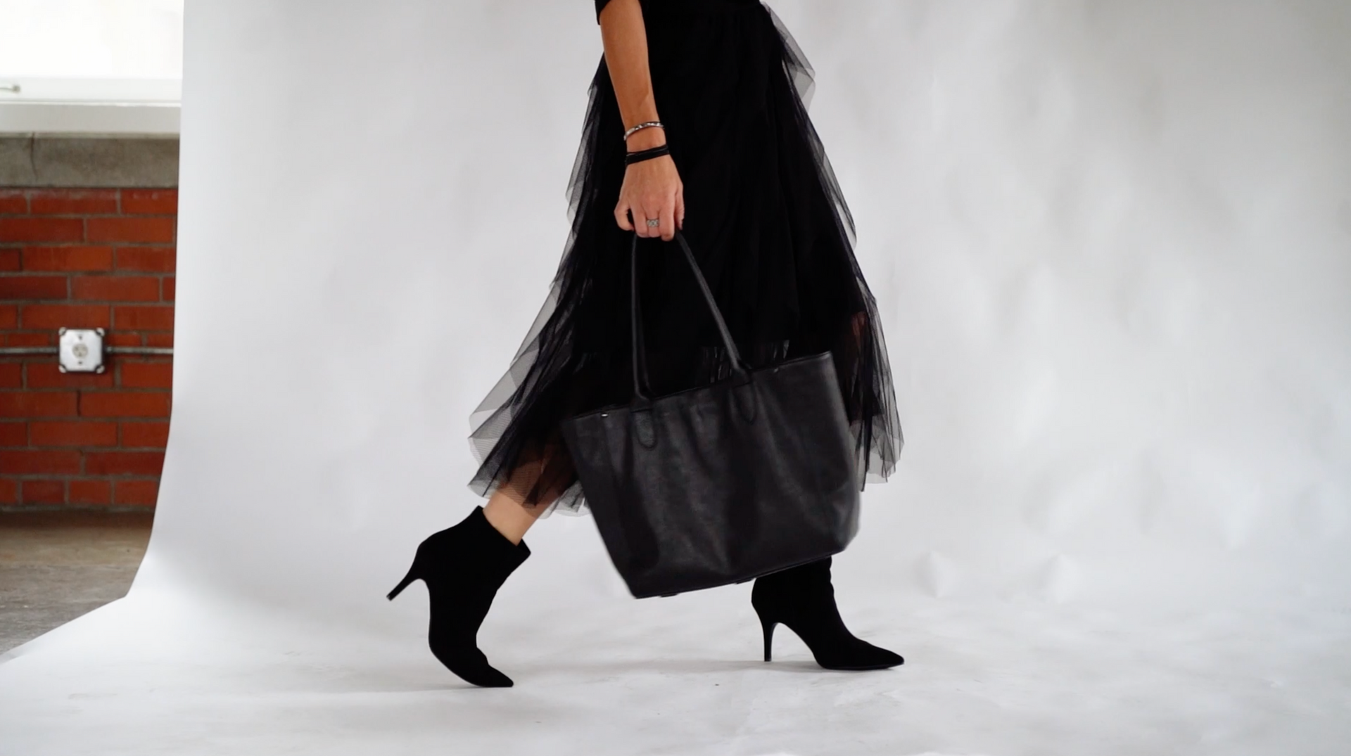 A woman in a black skirt is carrying a black tote bag.