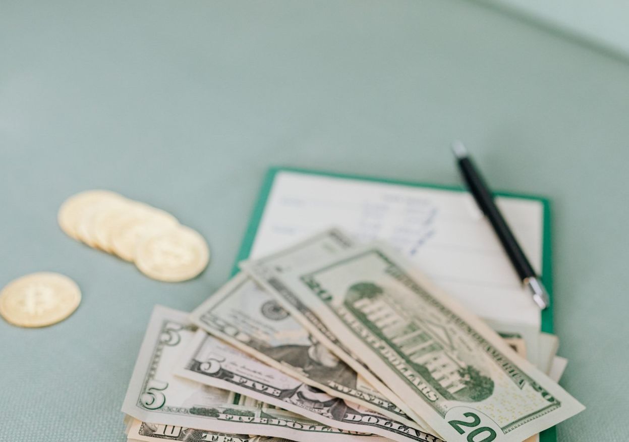 A pile of money and coins on a clipboard with a pen.