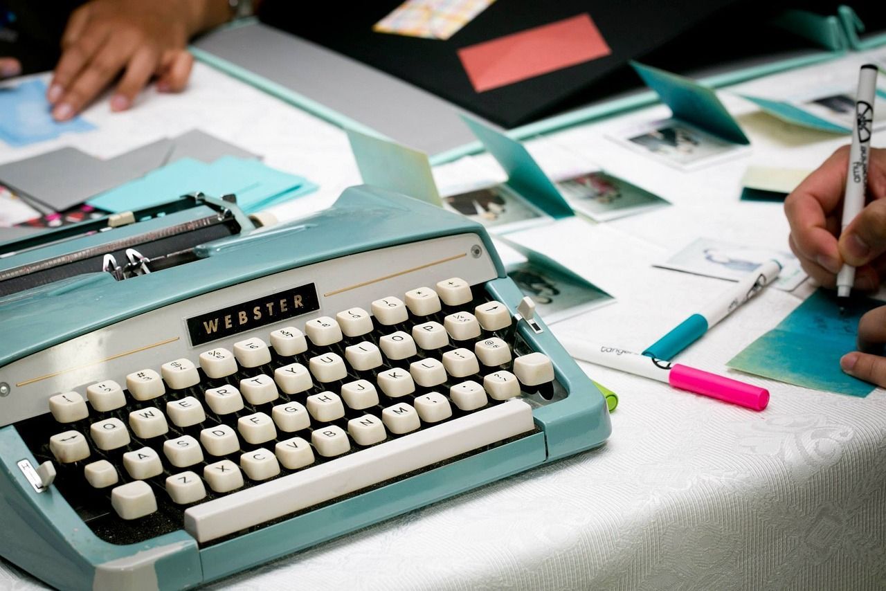 A person is writing on a piece of paper next to a typewriter.