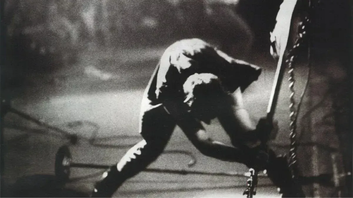 A black and white photo of a man smashing a guitar on a stage.