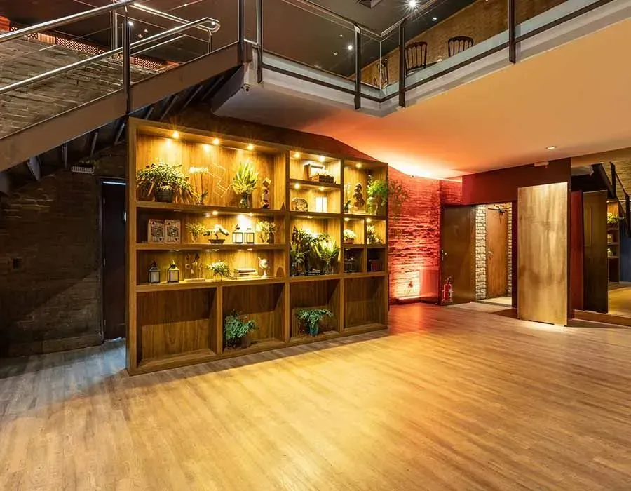 Modern loft lobby with warm wood floors, illuminated shelving, and staircase under mezzanine.