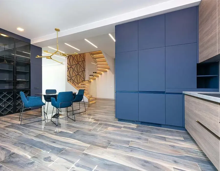 Modern dining area with blue chairs, marble floor, dark cabinetry, and a floating wooden staircase