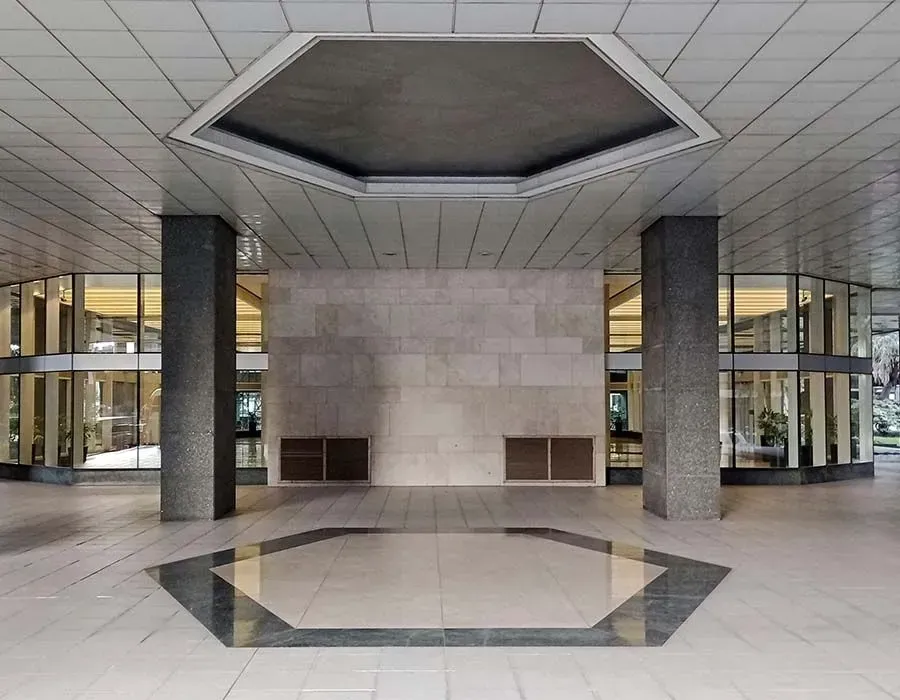 Modern building lobby with geometric stone floor, central pillar, and octagonal skylight ceiling