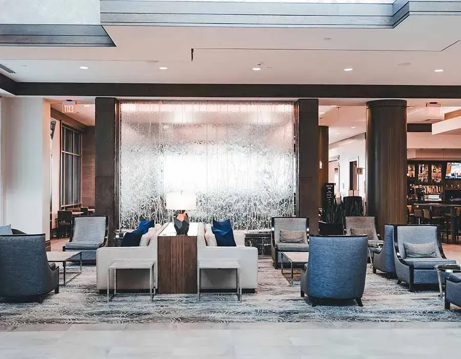 Modern hotel lobby with gray chairs, blue armchairs, and a large water wall backdrop