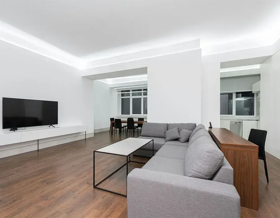 Modern living room with gray sectional, white walls, wood floors, TV, and dining area beyond
