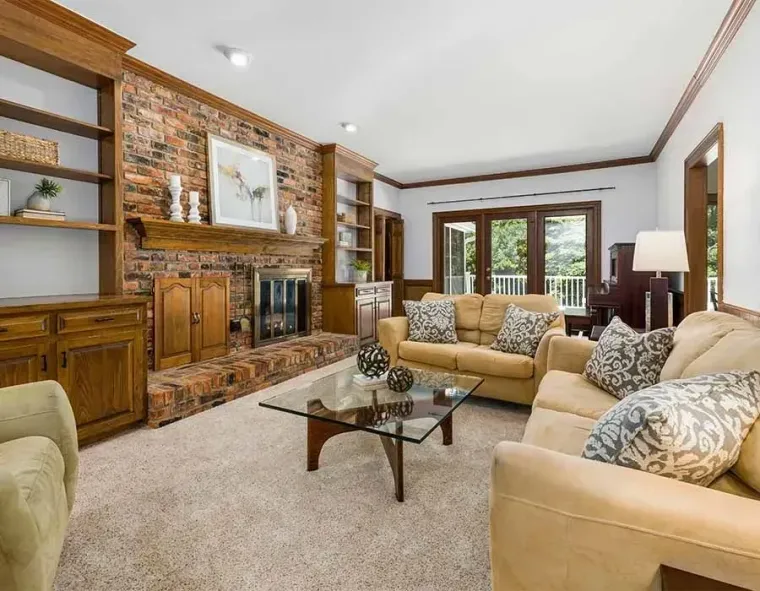 Bright living room with beige sofas, brick fireplace, glass coffee table, and French doors