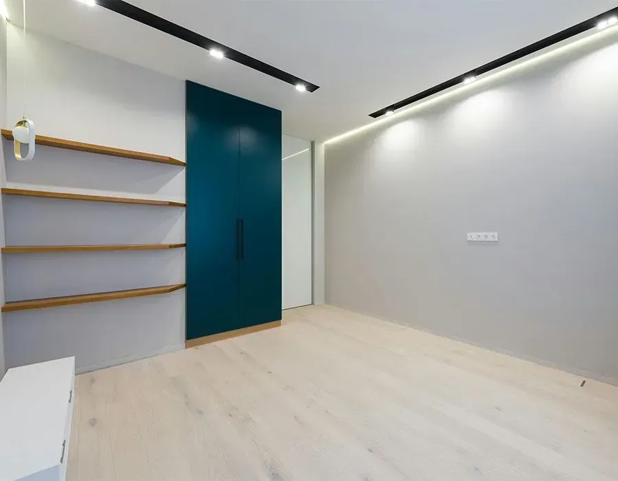 Minimalist empty room with light wood floor, teal door, floating shelves, and gray walls.