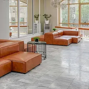 Modern lobby with tan leather seating, gray tile floor, large windows, and potted plants