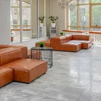 Modern lobby with tan leather seating, gray tile floor, large windows, and potted plants