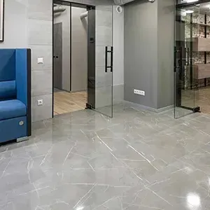 Modern office lobby with glass doors, gray walls, polished tile floor, and a blue sofa on the left