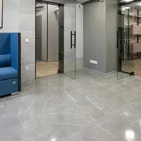 Modern office lobby with glass doors, gray walls, polished tile floor, and a blue sofa on the left
