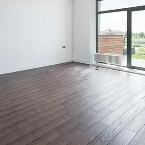 Empty modern room with dark wood floors, white walls, and a large glass door opening to a balcony.