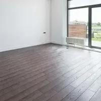 Empty modern room with dark wood floors, white walls, and a large glass door opening to a balcony.