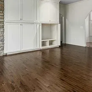 Empty room with dark hardwood floors and white built-in cabinets along one wall