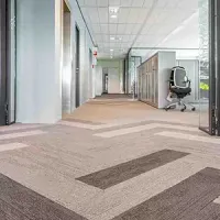 Modern office hallway with patterned carpet, glass walls, and a rolling chair on the right.
