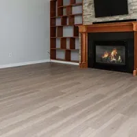 Empty living room with light wood floors, fireplace, and built-in shelving beside a TV
