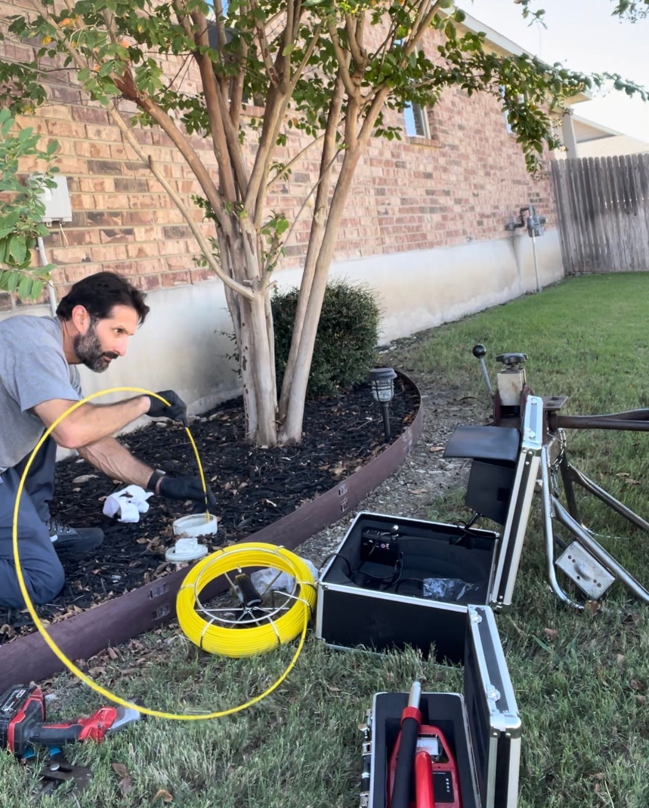 A man is kneeling down in a yard with a yellow hose.
