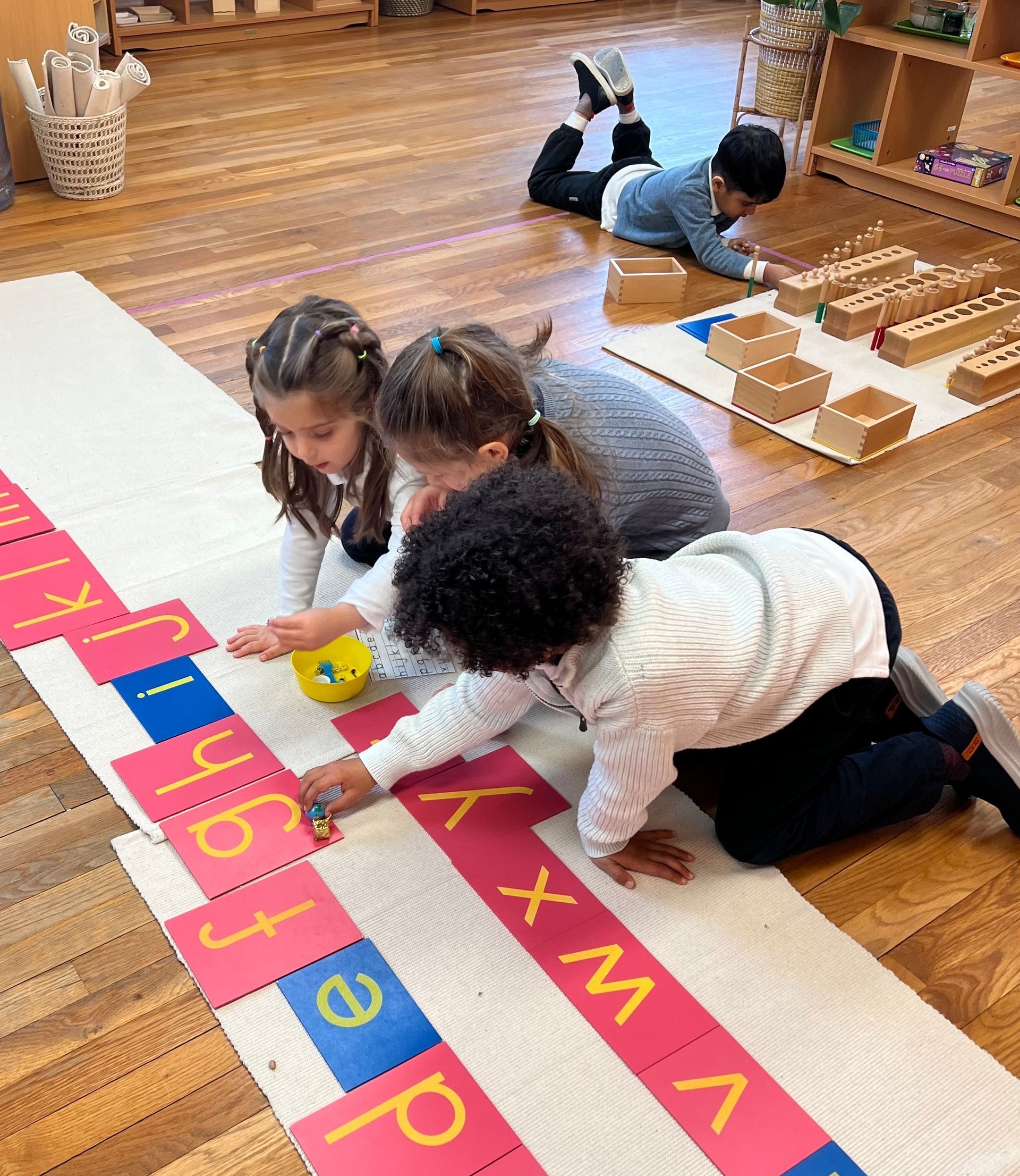 A group of children are playing with alphabet cards in a Montessori classroom.