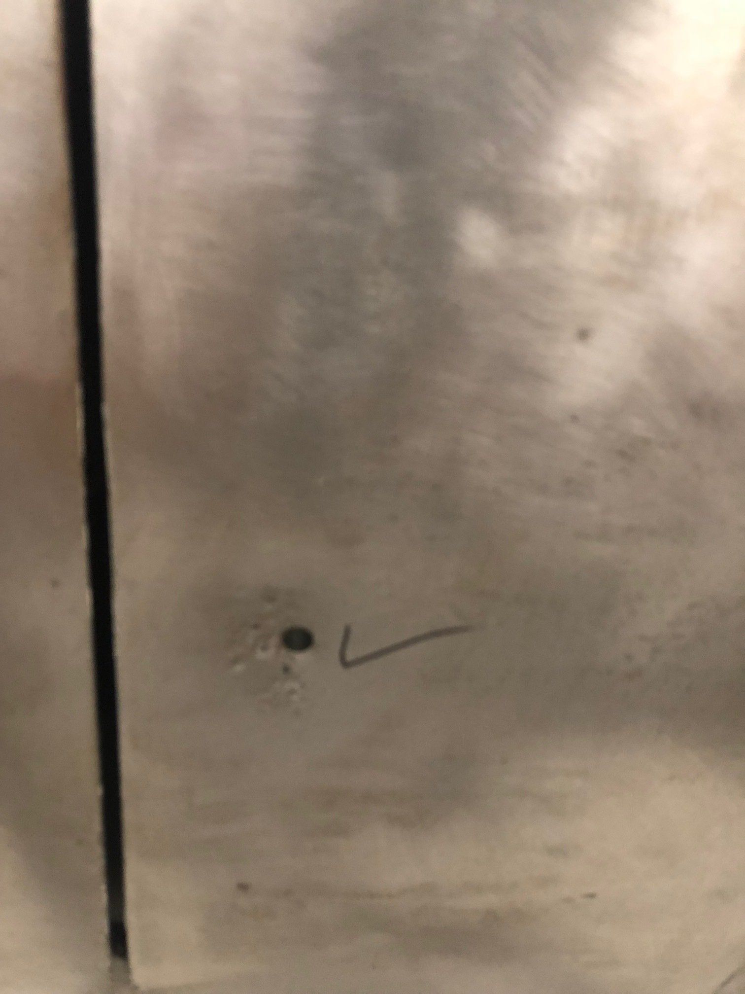 Close-up of a stainless steel surface with a small hole and a black check mark.