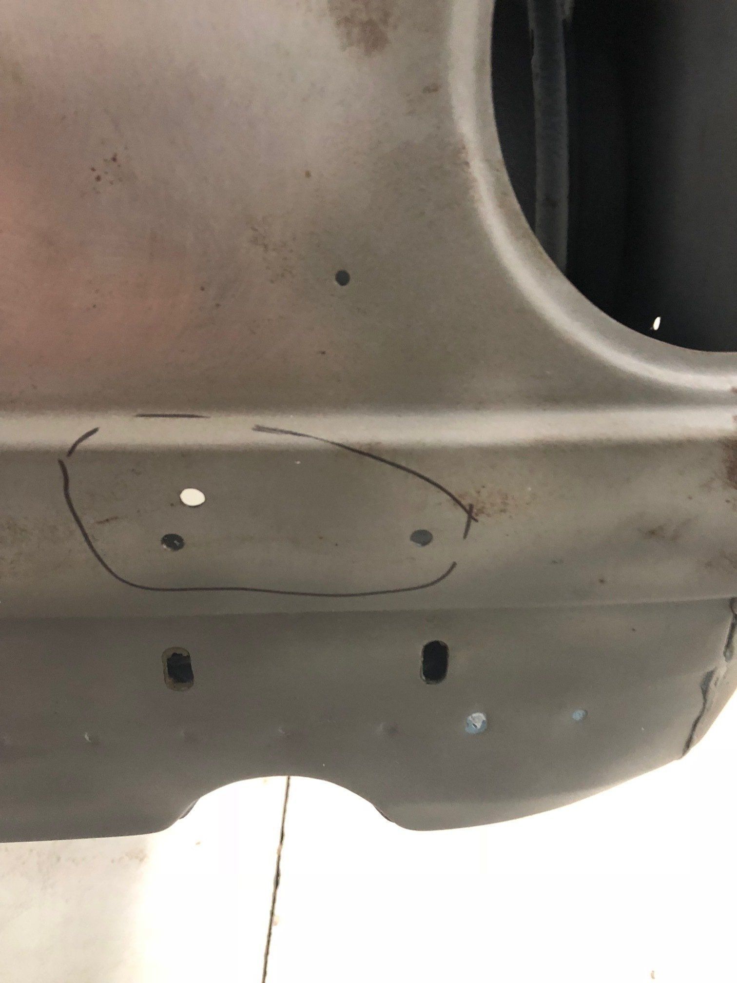 Close-up of a gray car bumper with a marked oval around two holes and a small dent