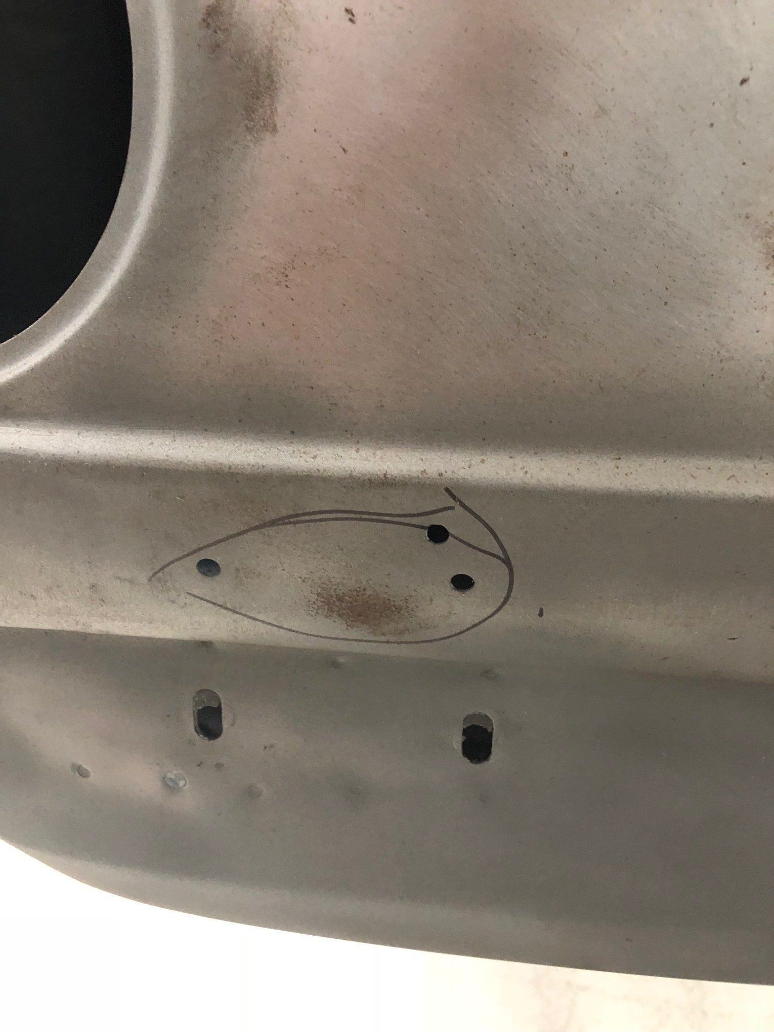 Close-up of a silver metal panel with scratches, dark spots, and small holes near the edge.