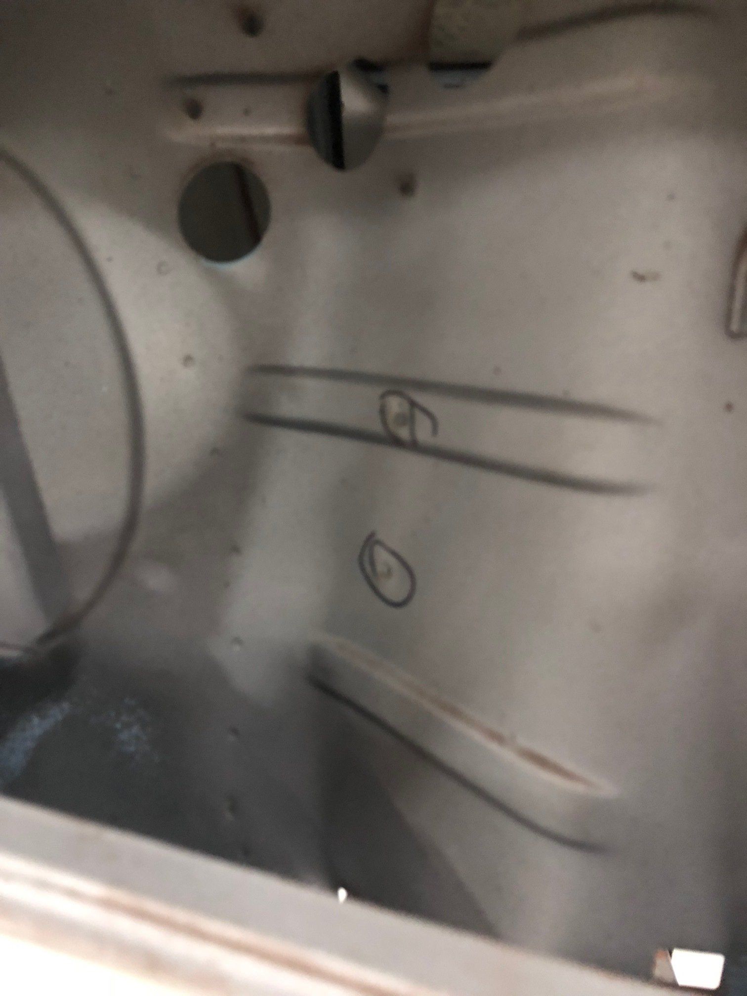 Interior of a white metal compartment with circular openings and marker scribbles on the wall