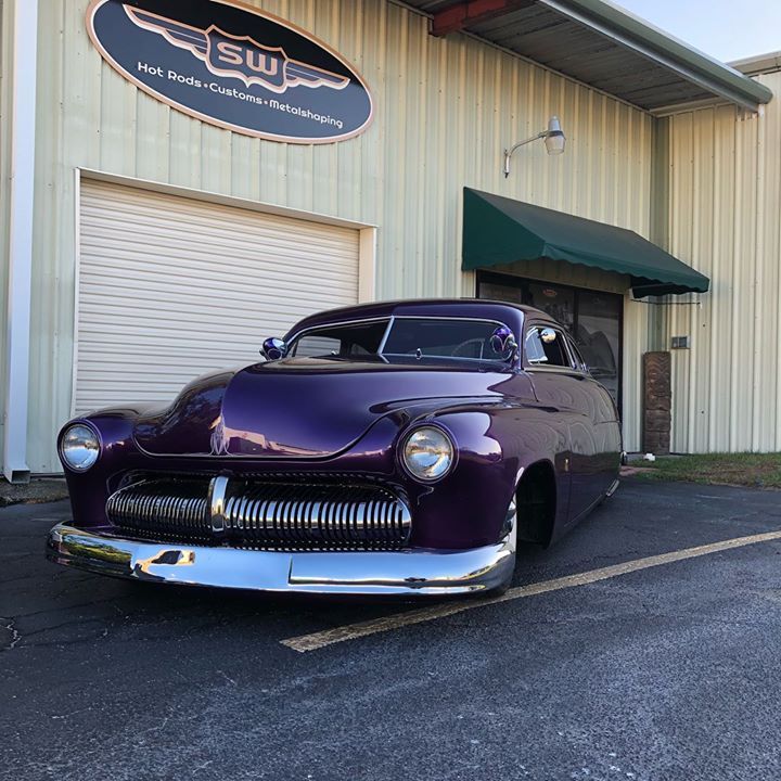 Purple classic car parked outside a metal building with a green awning