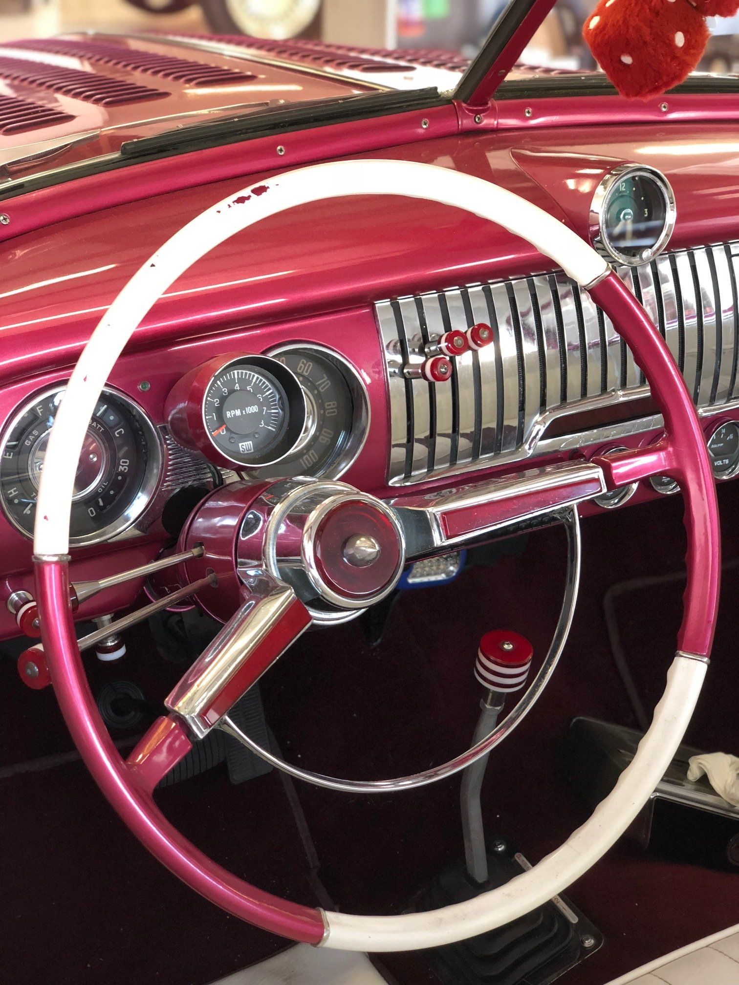 Pink and white vintage car dashboard with chrome trim and a white steering wheel
