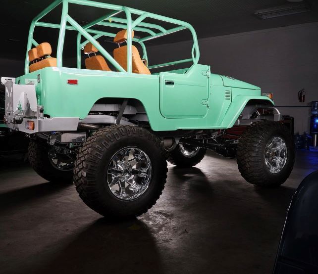 Mint-green lifted off-road jeep with orange seats in a dark garage, side view