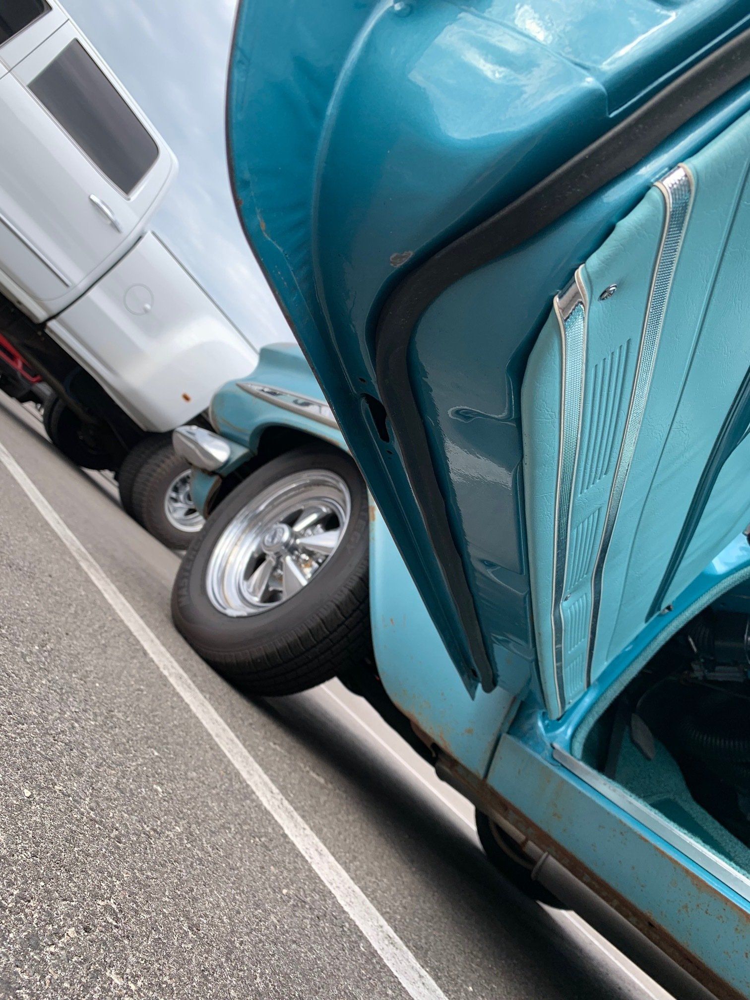Teal car parked close to a white truck on a roadside, with the car door open.