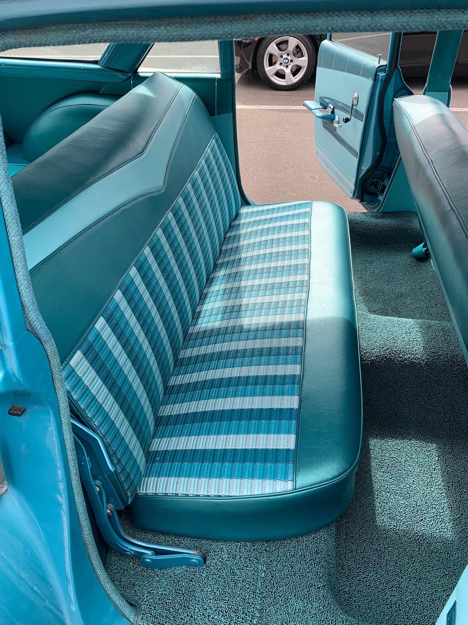 Teal-striped car bench seat and matching interior on a turquoise carpet, viewed from the open door
