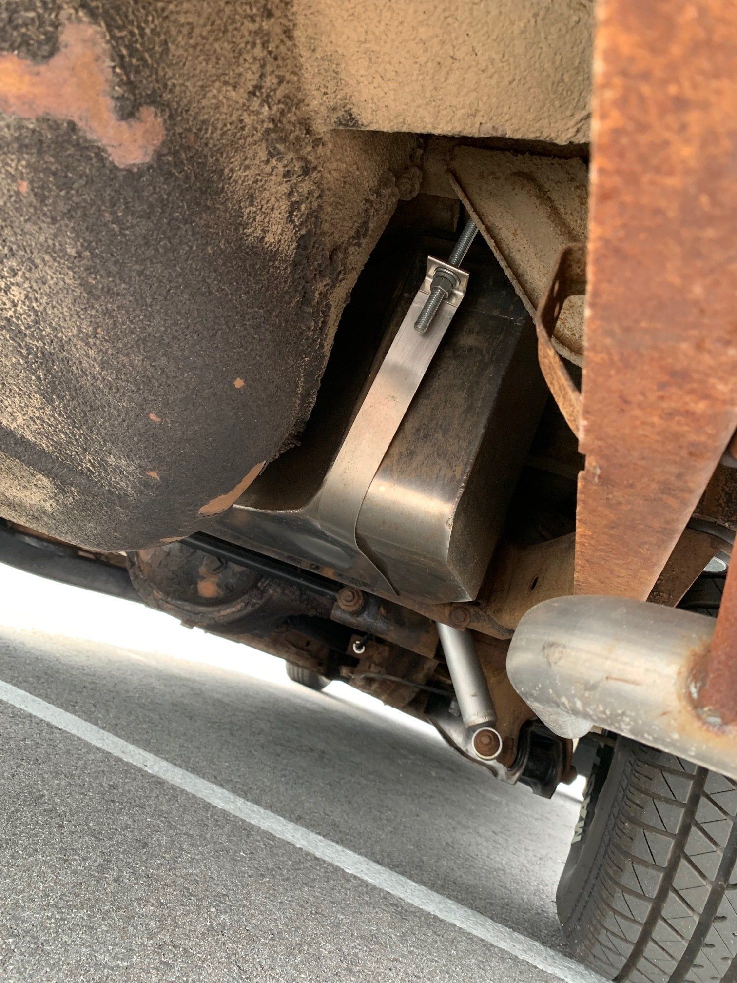 Undercarriage of a vehicle showing a metal component and rear tire on a road.