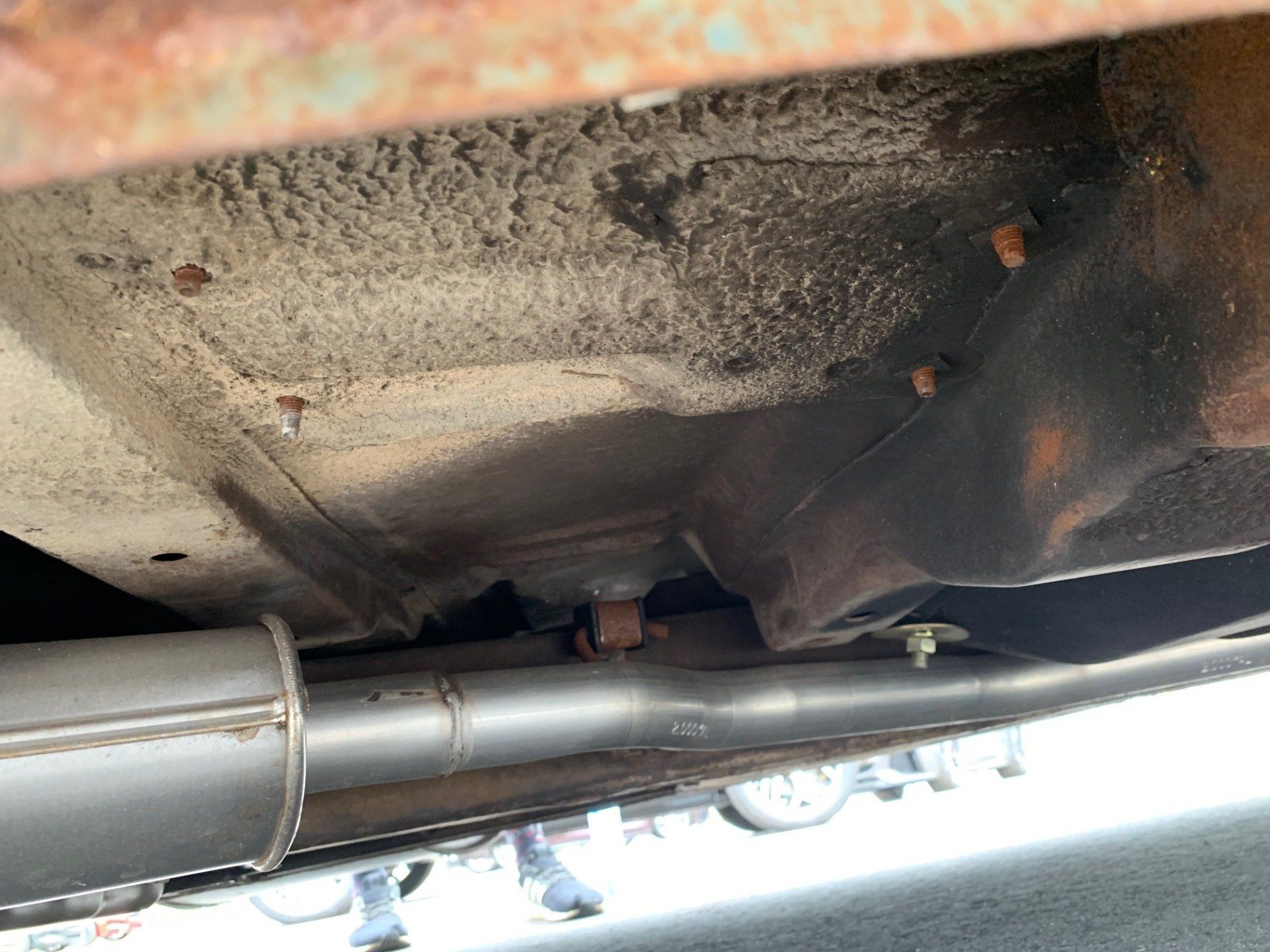 Undercarriage of a car with a rusty exhaust and a dirty, heat-stained floor pan