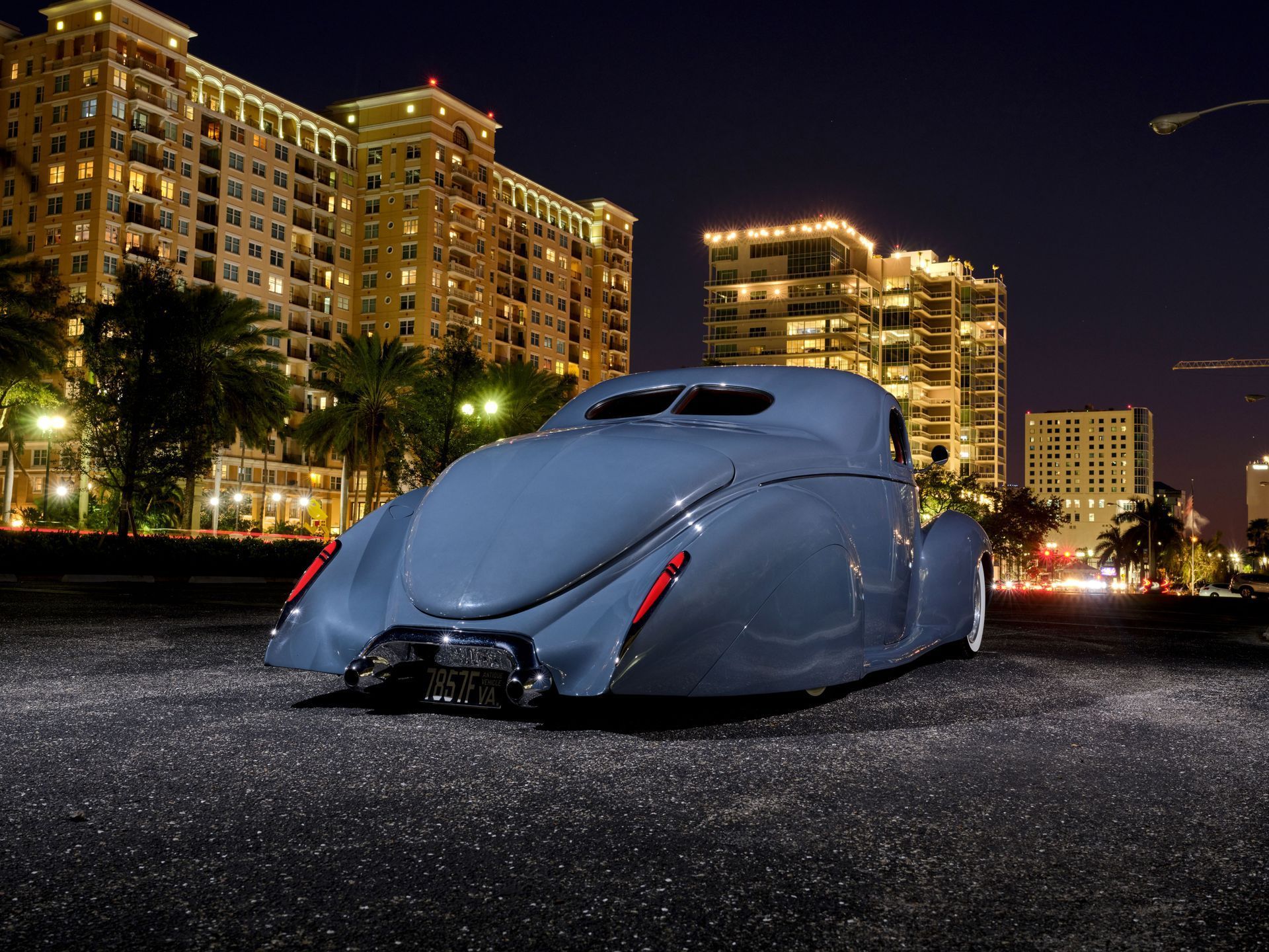 Streamlined vintage car on a street at night with lit high-rise buildings in the background