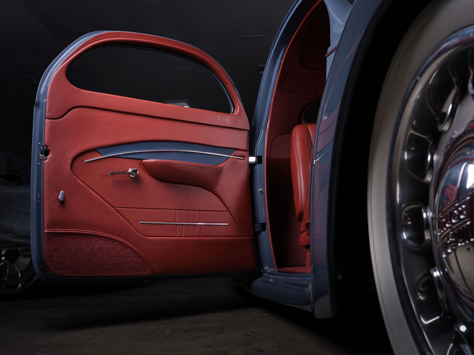 Open car door with red leather interior and a chrome wheel in a dark setting