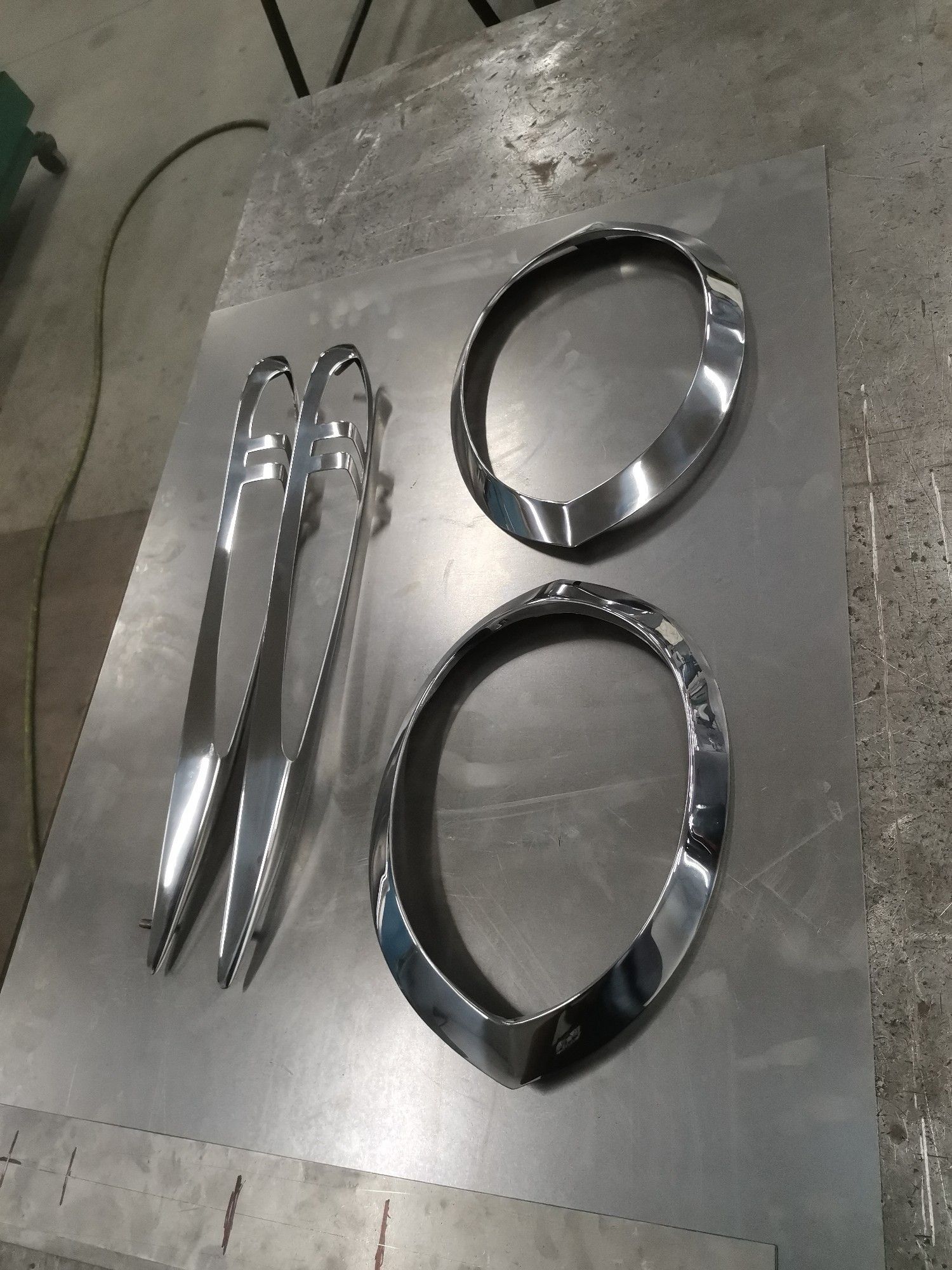 Two chrome oval trim rings and two metal clips on a workbench, viewed from above