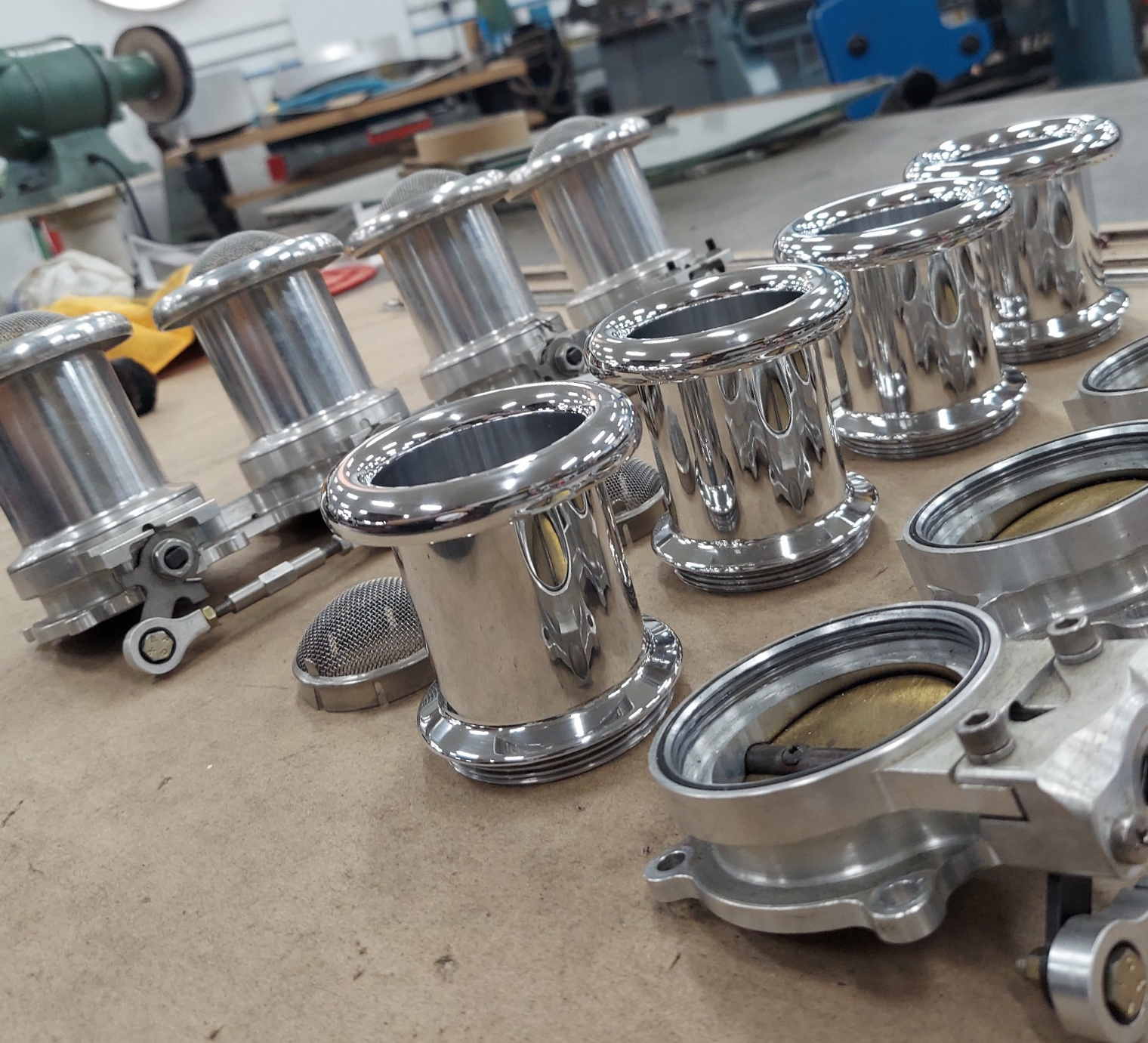 Polished metal industrial parts arranged on a workshop floor, with machinery blurred in the background