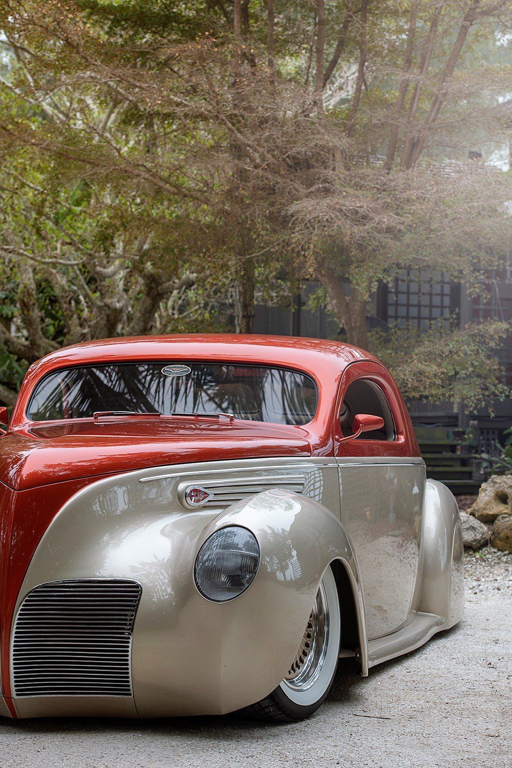 Low-slung custom vintage car with red roof and silver body parked outdoors by trees