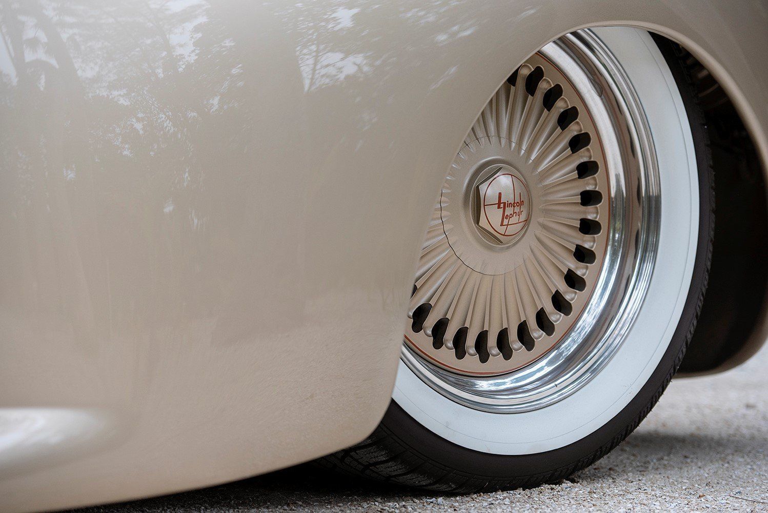 Close-up of a cream-colored car wheel with chrome hubcap and whitewall tire tucked under the fender