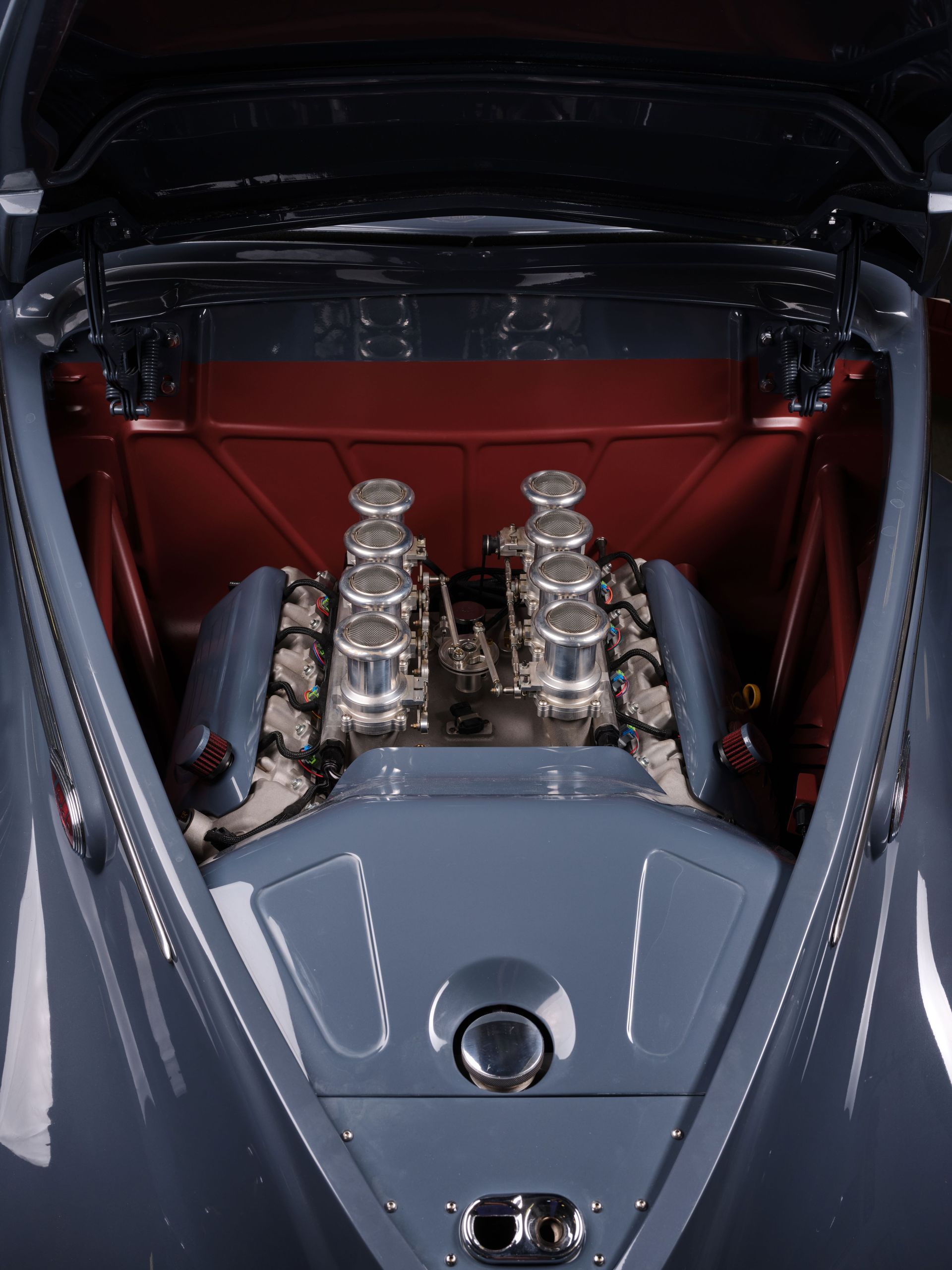 Classic car engine bay with polished chrome intake stacks and a red interior panel.