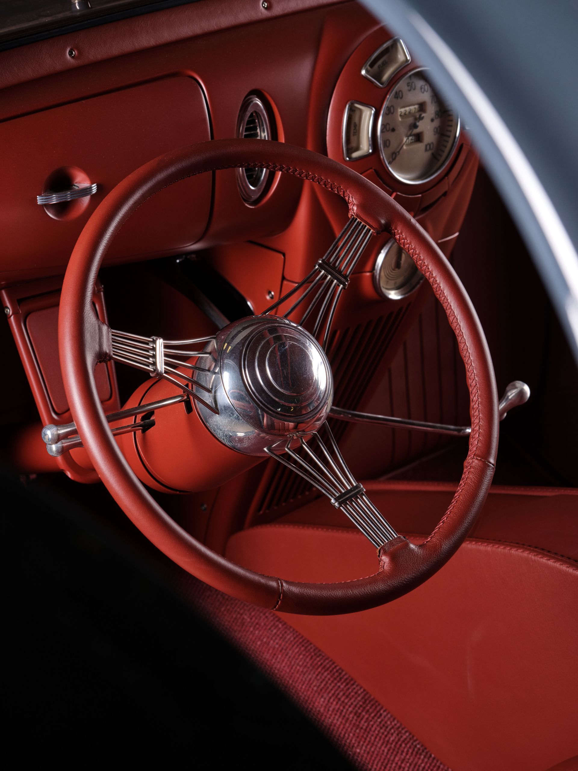 Red vintage car dashboard with a chrome steering wheel and round gauges