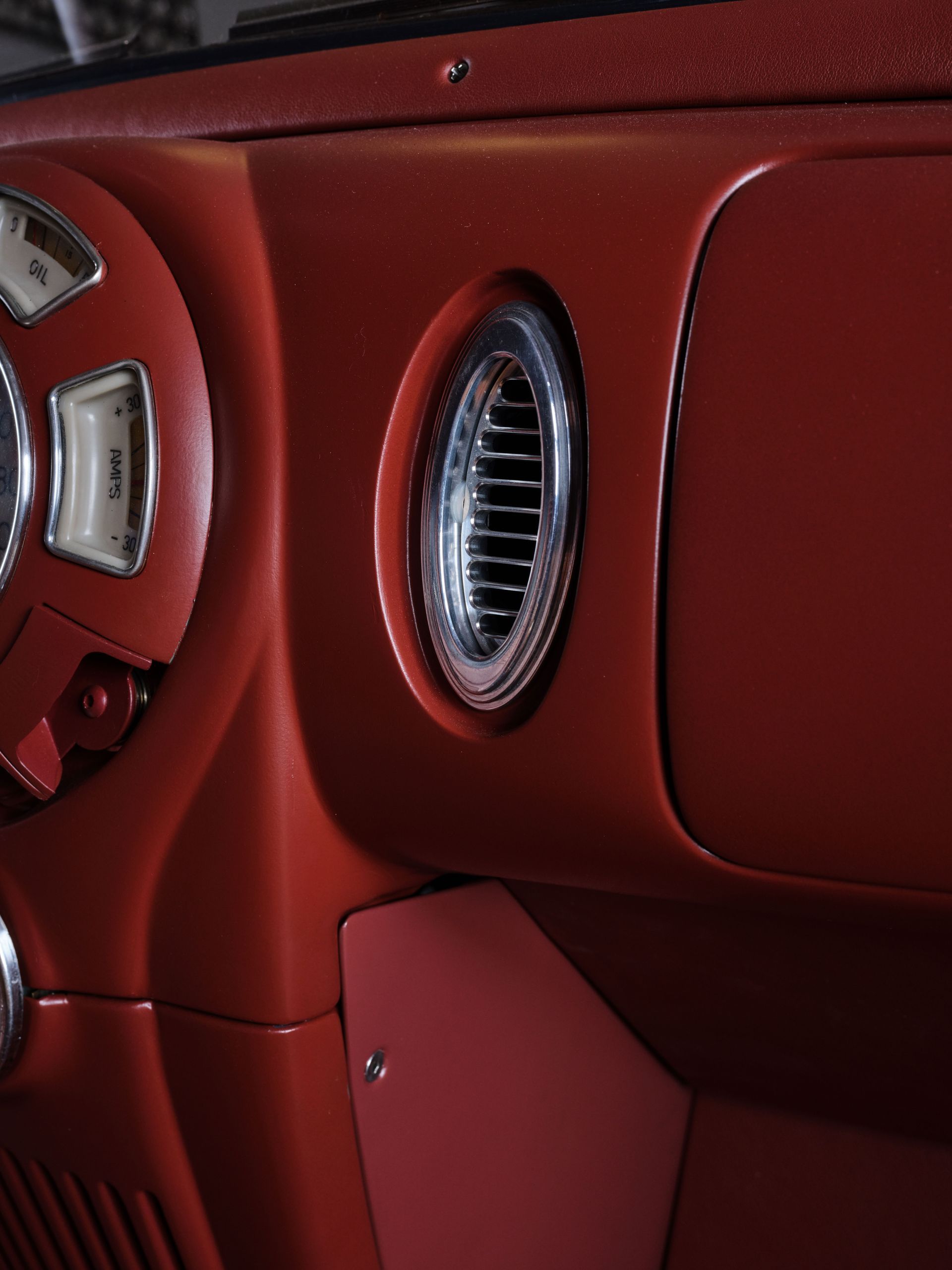 Red leather car dashboard with a chrome oval air vent and part of a steering wheel.