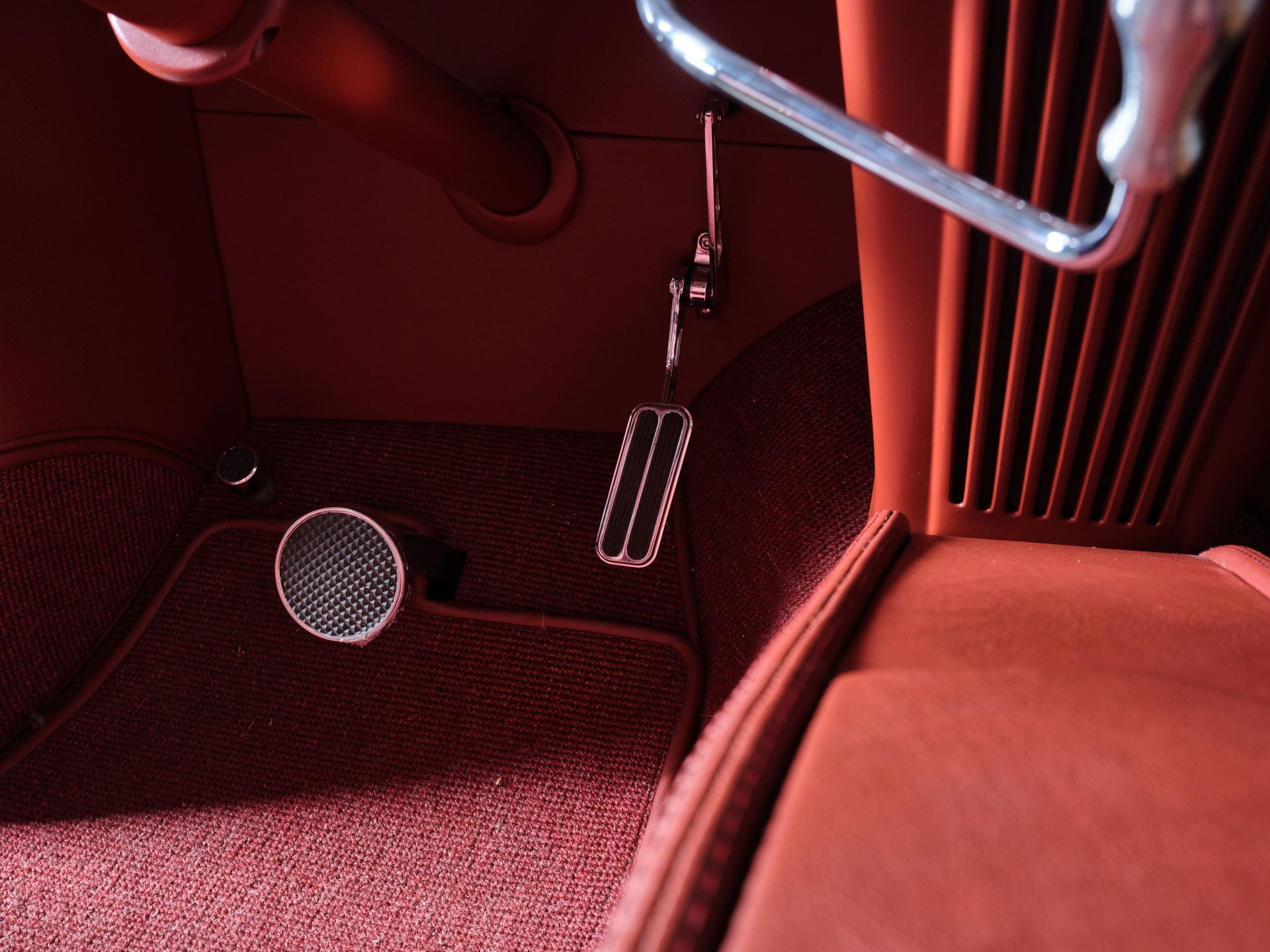 Red car interior with hanging pedals and a footrest on the floor mat.