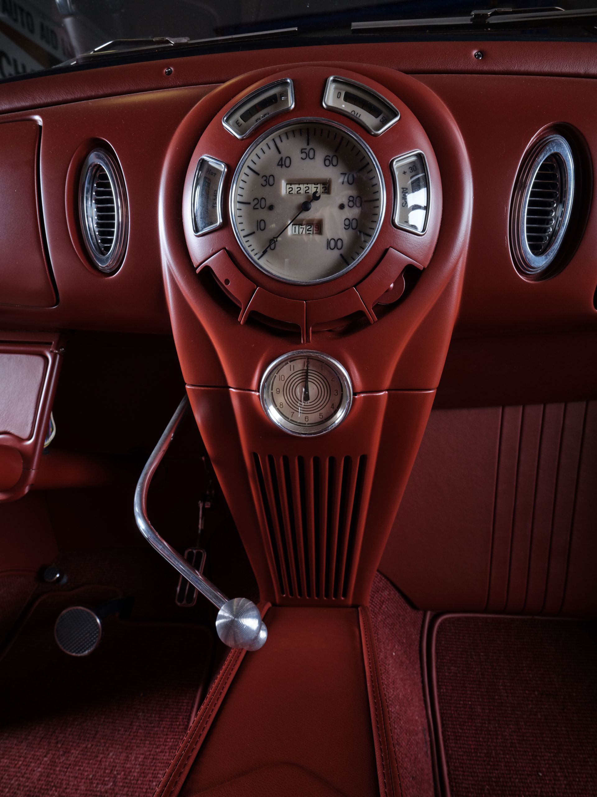 Vintage red car dashboard with chrome center clock and gauge cluster, viewed from the driver’s seat