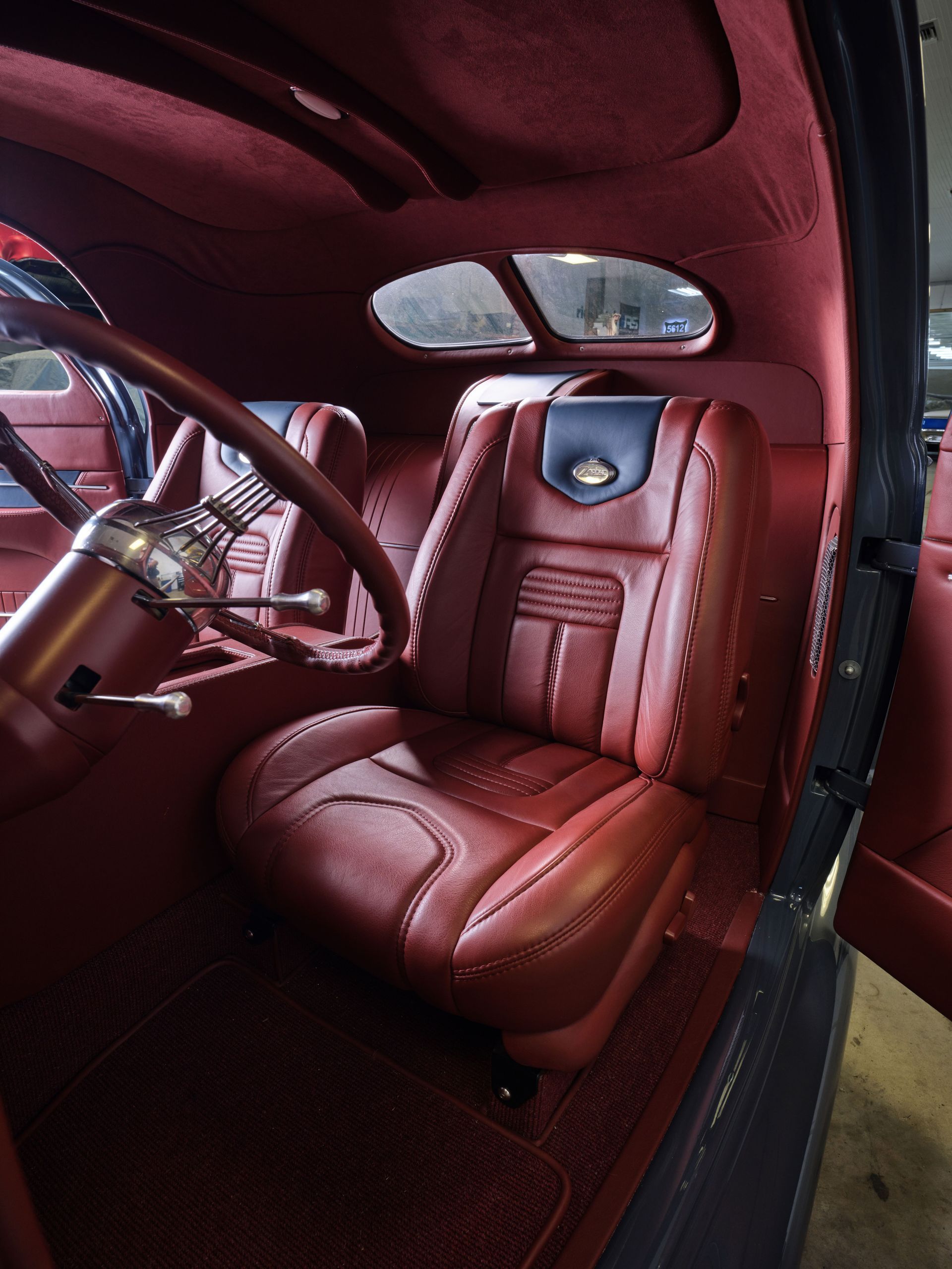 Luxurious burgundy car interior with red leather driver’s seat and chrome steering wheel